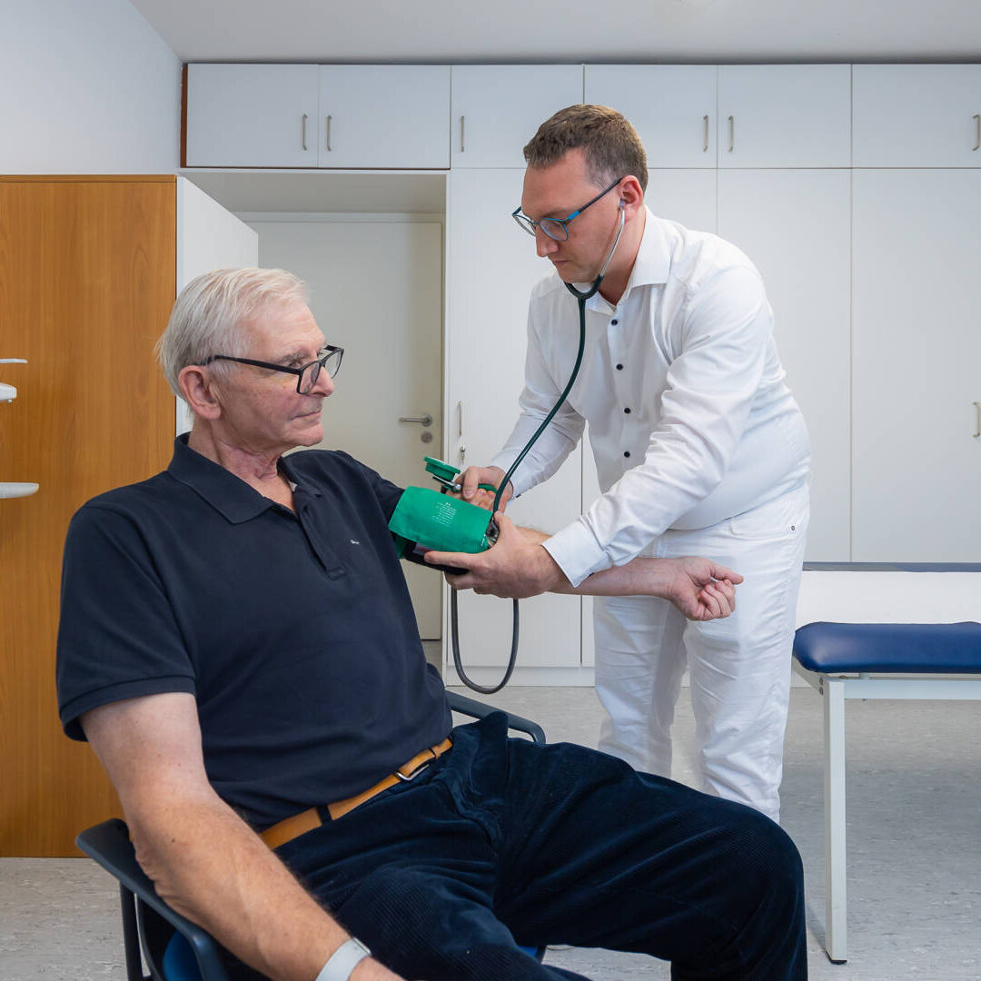 Dr. Matthias Hartmann misst den Blutdruck einen älteren Mannes im Behandlungszimmer