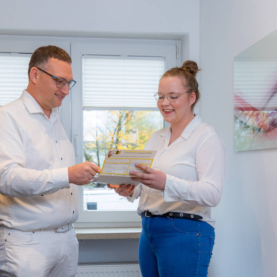 Dr. Matthias Hartmann und eine Angestellte stehen im Praxisflur und schauen auf ein Dokument