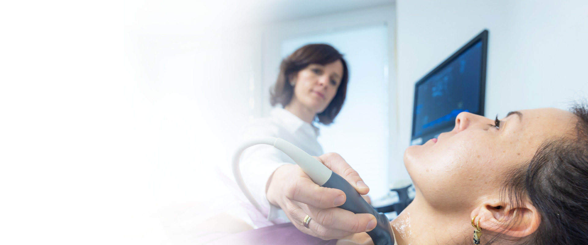 Dr. Carola Hummel untersucht eine junge Patientin im lila Pullover mit einem Ultraschallgerät am Hals