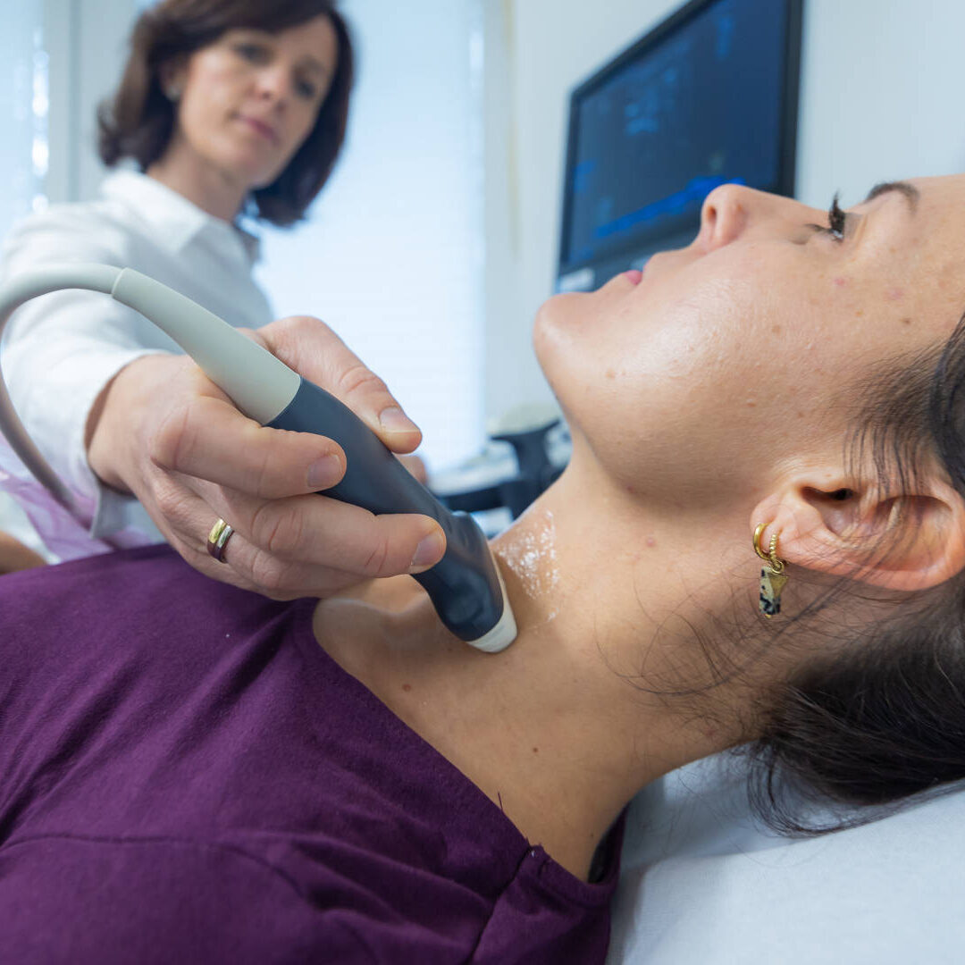 Dr. Carola Hummel untersucht eine junge Patientin im lila Pullover mit einem Ultraschallgerät am Hals