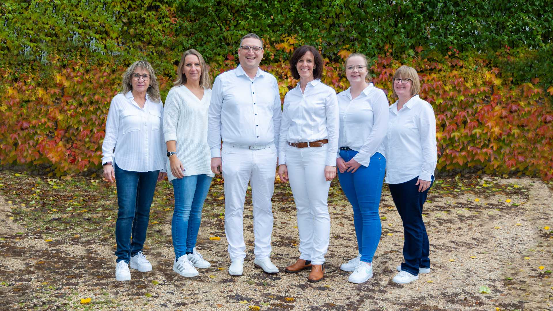 Das ganze Praxisteam steht vor einer bunten Herbstlicher Pflanzenwand